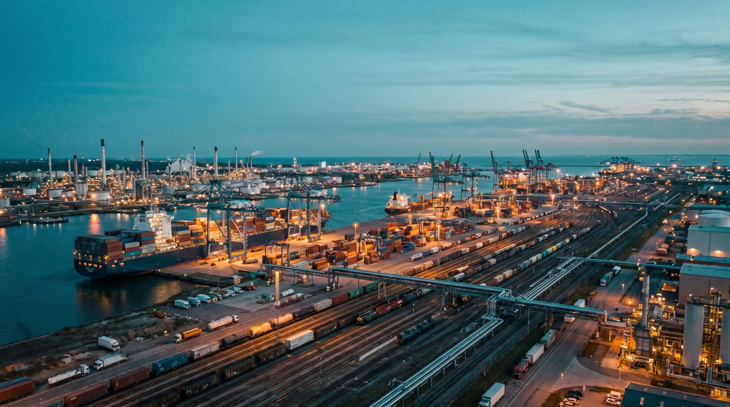 Containerterminal bei Nacht mit beleuchteten Kränen und gestapelten Containern.