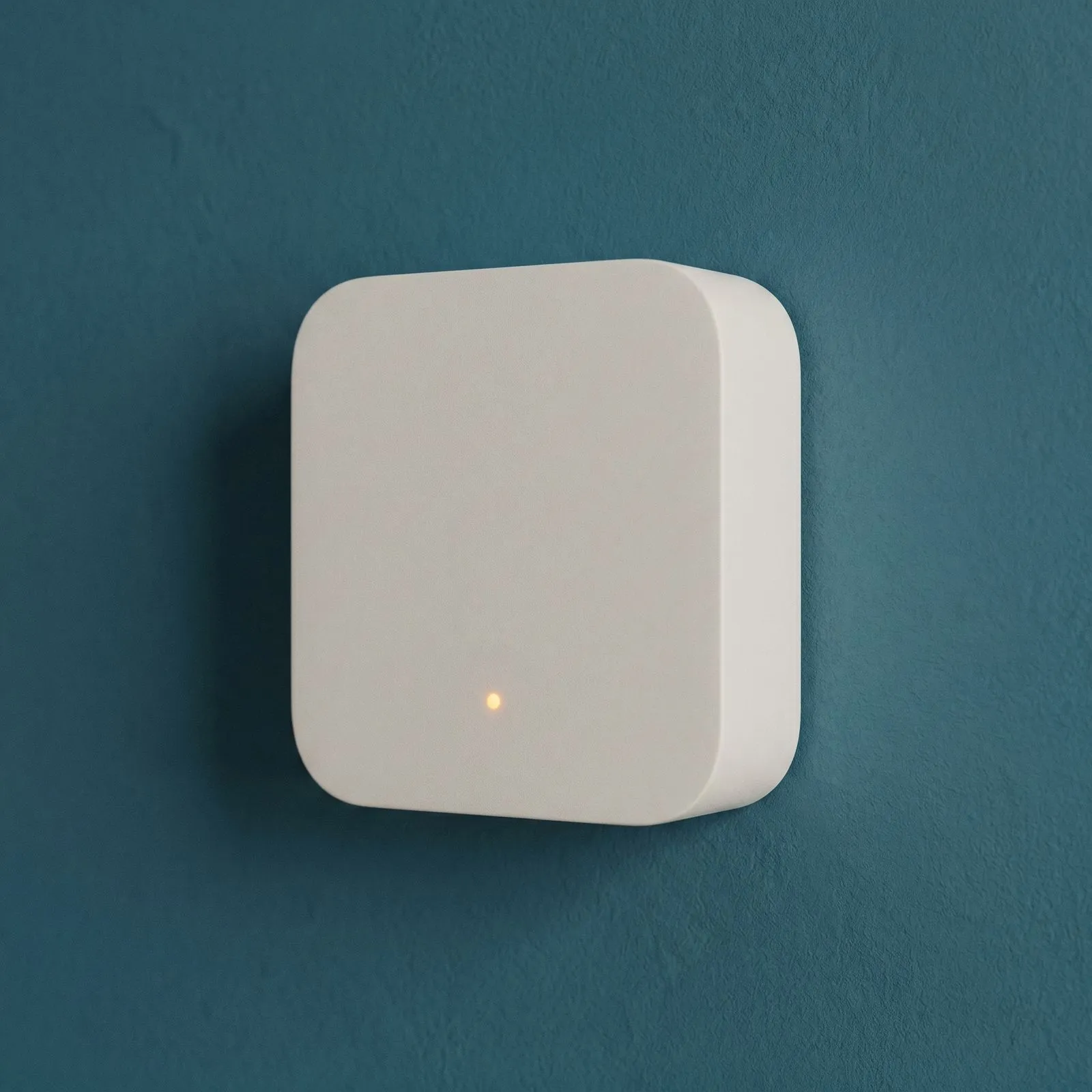 Weißes Smart-Meter-Gateway mit leuchtender Statusanzeige an einer Wand.