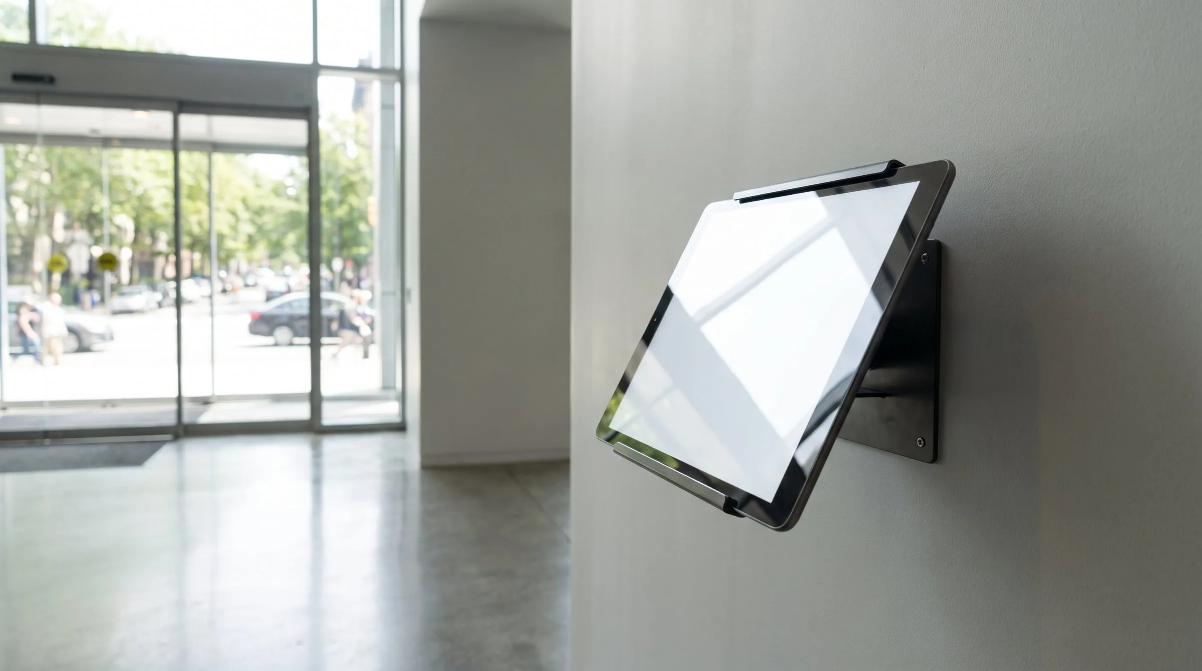 Wandhalterung mit Tablet im Foyer eines Gebäudes, im Hintergrund die verglaste Eingangsfront.