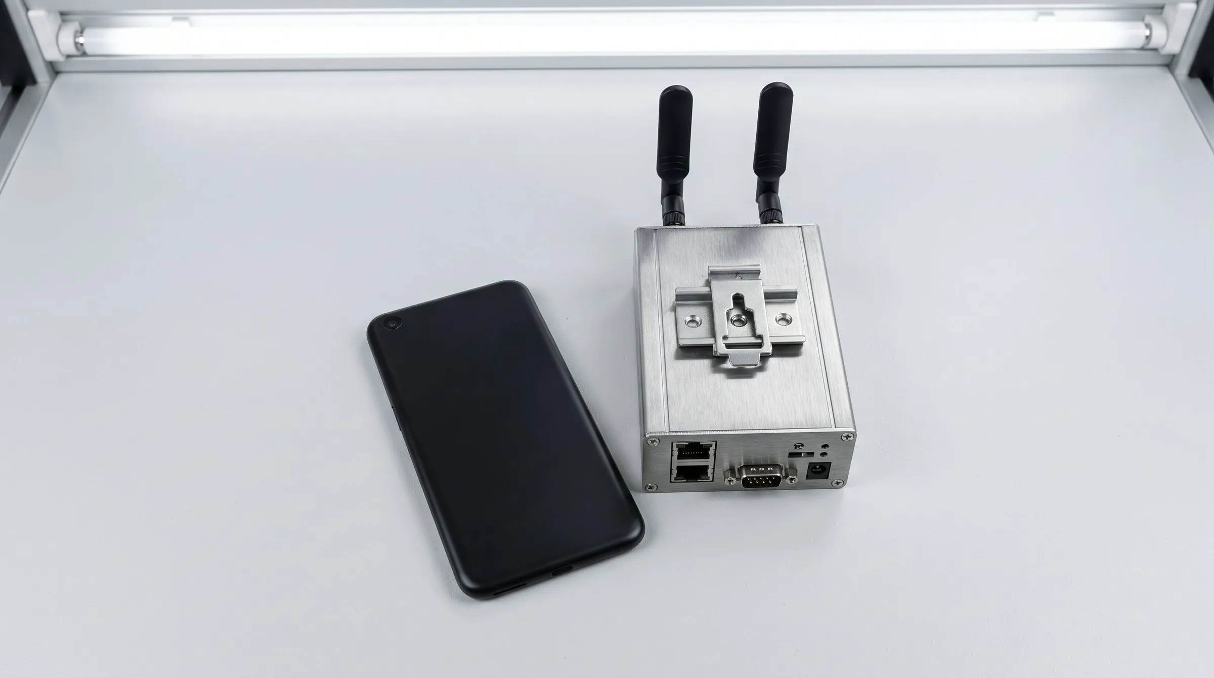 Ein Smartphone liegt neben einem Industriemodem mit zwei Antennen auf einer hellen Arbeitsfläche.